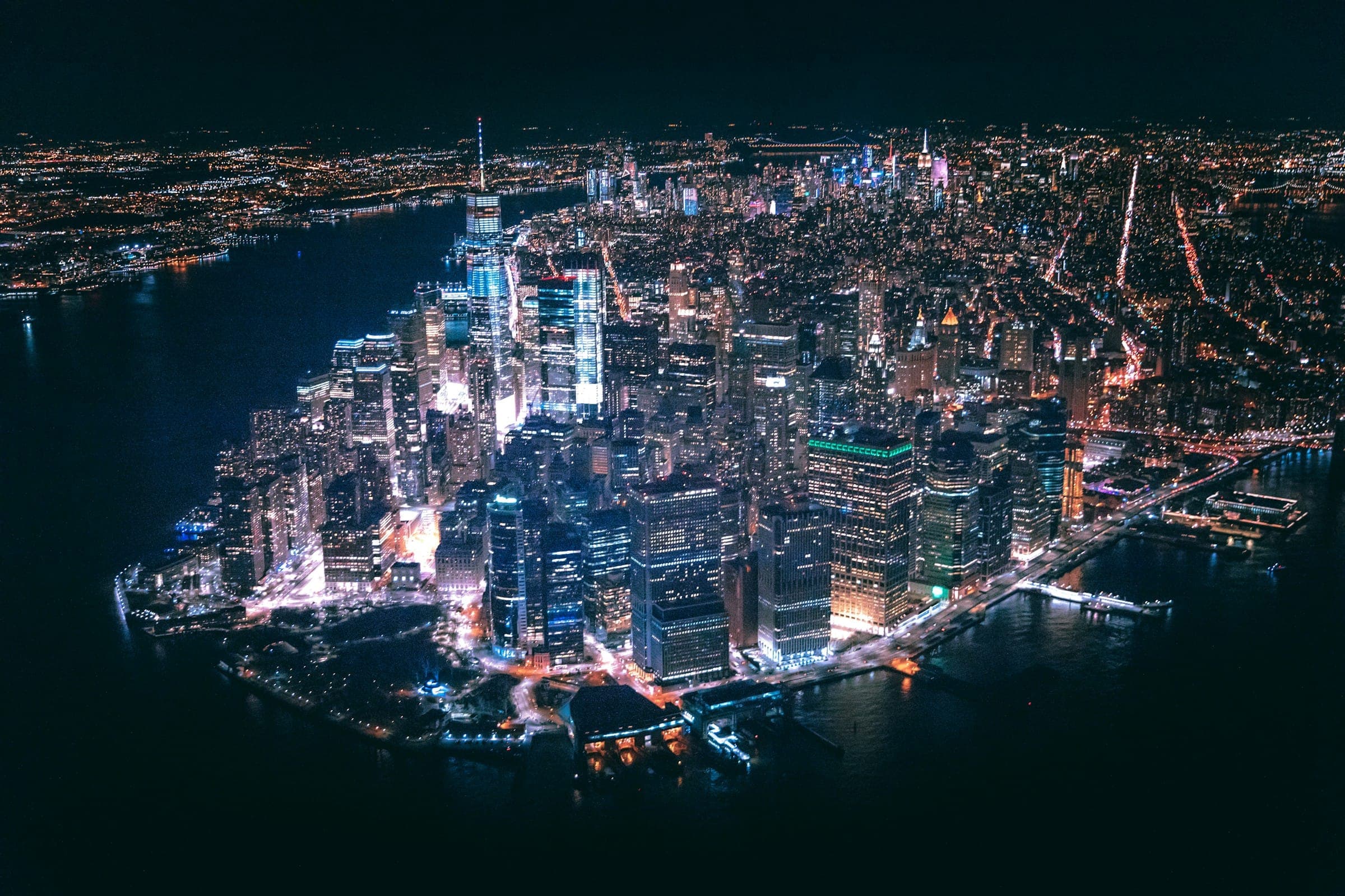 Aerial view of Lower Manhattan lit up at night, surrounded by dark water